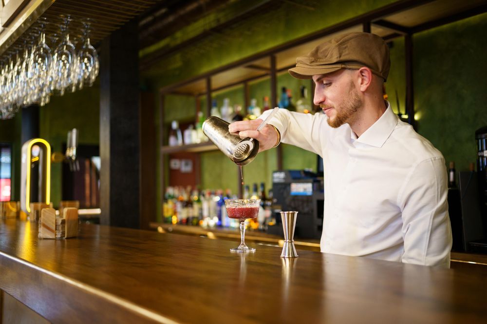 Man working in bar pouring cocktail from shaker into glassware