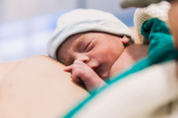 Cute newborn baby sleeping laying on his mother in the hospital room.