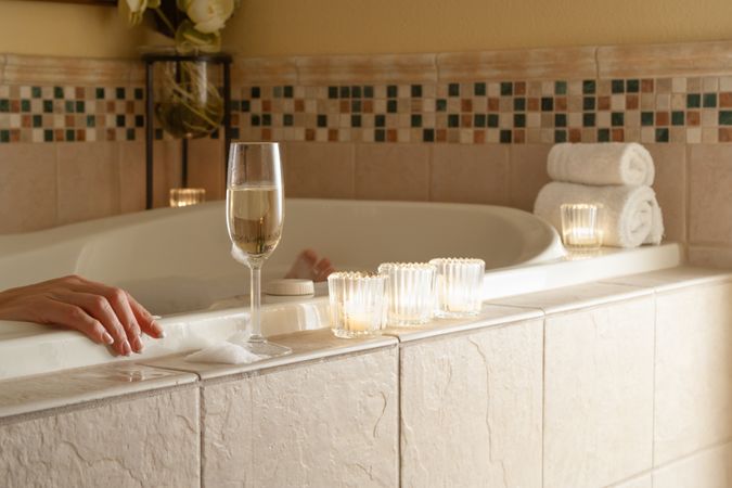 Woman Relaxing in the Bathroom Spa Tub with a Glass of Sparkling Champagne and Candles.