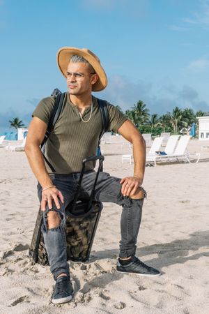 Close up of a traveler hipster man sitting on the carrying baggage, beautiful beach, enjoying amazing view.