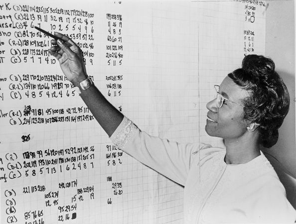 Shirley Chisholm, Congresswoman from New York, looking at list of numbers posted on a wall, 1965