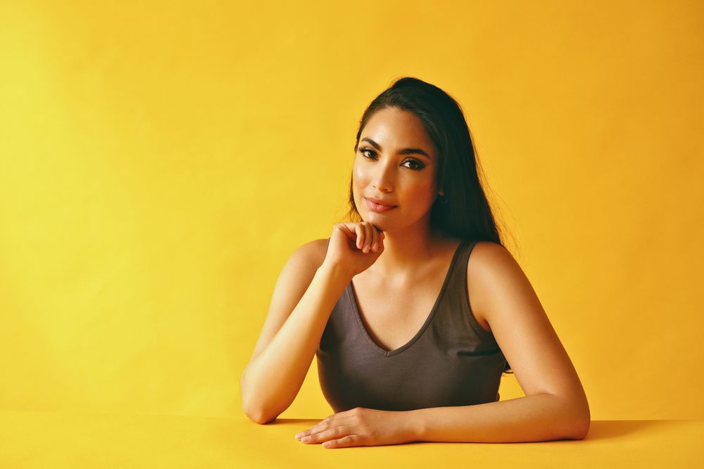 Serious Hispanic woman looking at camera and sitting in yellow room, copy space