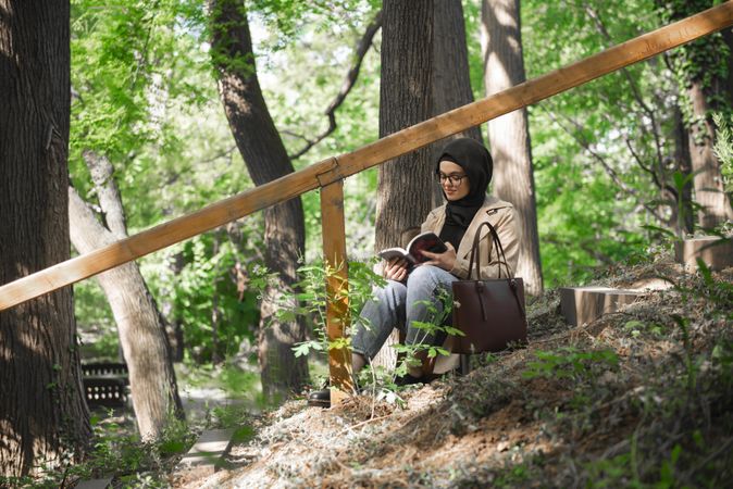 Muslim woman calmly reading a book on park stairs