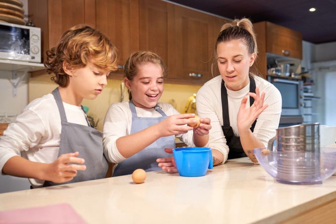 Mother helping kids to make dough in kitchen