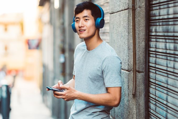 Content Asian man in headphones listening music on smartphone on street
