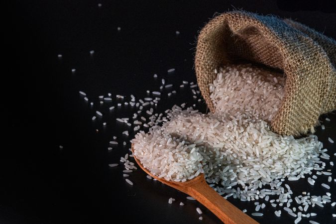 rice spilling from a burlap sack onto a dark surface