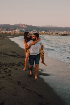 Amorous man carrying woman on arms along sandy beach