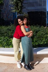 Female couple holding each other in city park with office buildings in background
