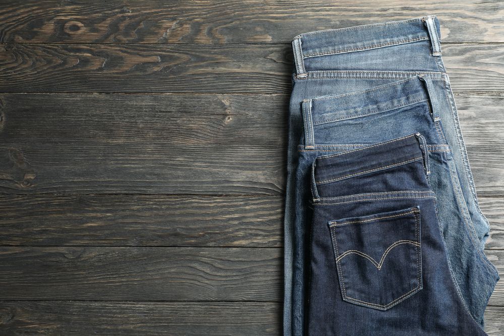 Different jeans folded on a wooden background, space for text