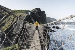 Man crossing rope bridge leading to rocky island