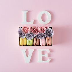 The word “Love” surrounding box of macarons and flowers on pink background