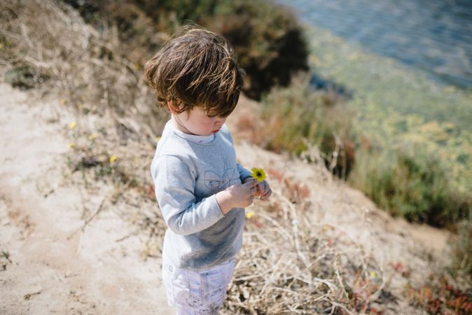 Child looking at flower in hands in mountains with interest