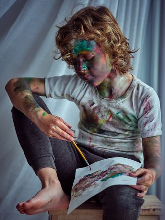 Boy with arm put on knee holding paintbrush and drawing