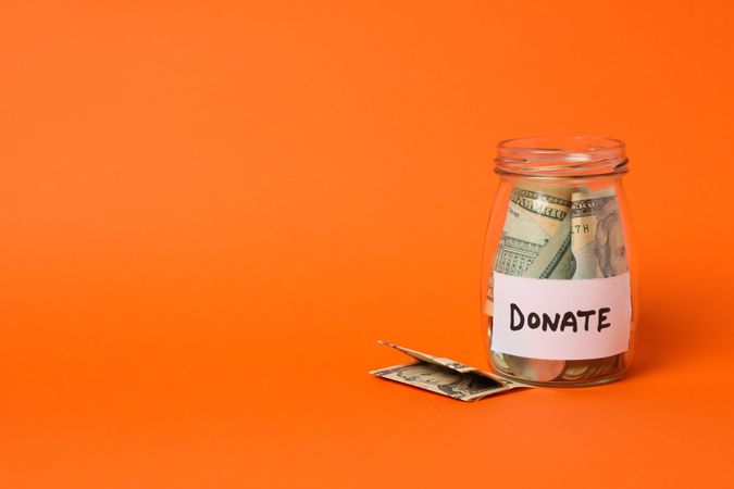 Glass jar with money and text Donate on orange background