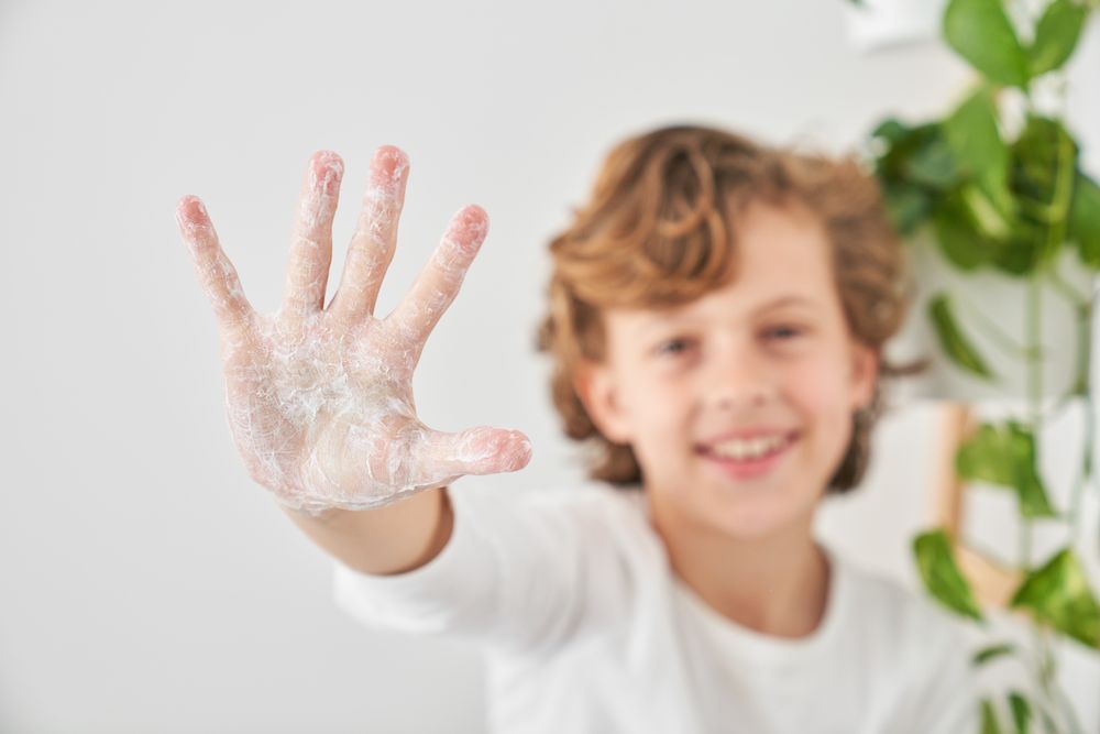Content boy showing hi gesture with soapy hand