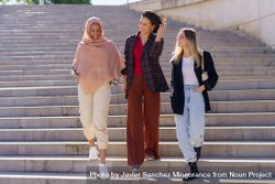 Female friends descending outside staircase and talking on sunny day 0JX184
