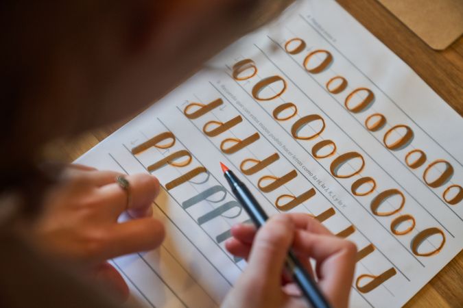Crop person practicing lettering using orange felt pen