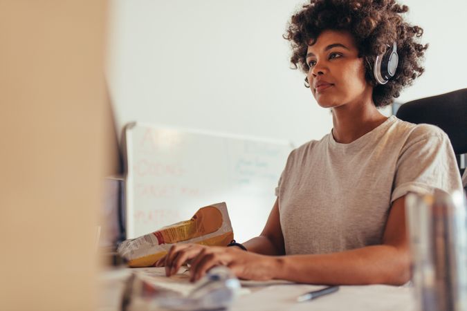 Focused woman wearing headphones concentrating while working on computer at tech startup