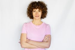 Calm female in light pink t-shirt standing with arms crossed in blank space
