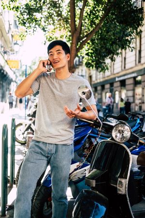 Confident Asian man talking on phone while standing by motorbike
