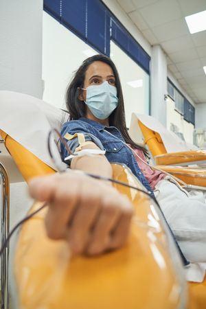 Woman in blue mask donating blood in donation center
