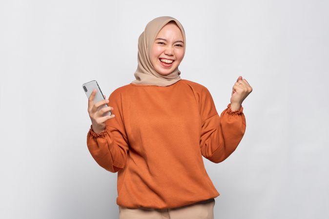Muslim woman celebrating while holding her smartphone