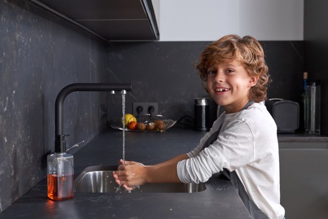 Delighted boy washing hands in kitchen