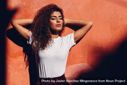 Arab woman with curly hair standing in the sun with her eyes closed and arms up bYLlg4