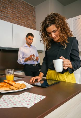 Woman looking at tablet while having quick coffee at home before work