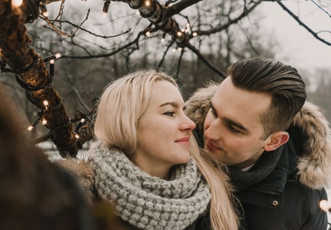 Smiling couple having fun on street near tree with fairy lights