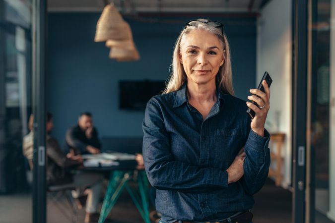 Portrait of older woman holding a phone standing in office