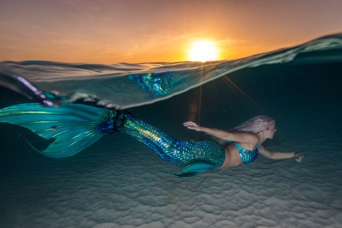 Blond fairytale female mermaid swimming along sea bottom