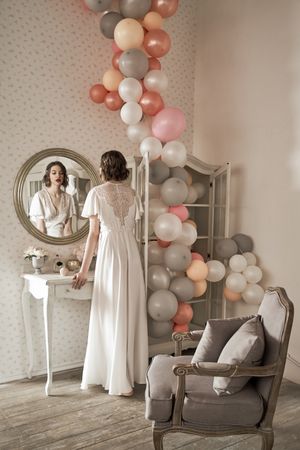 serious young woman standing and looking in big round mirror in boudoir