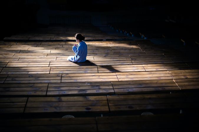 Back view of person in blue robe sitting on brown wooden floor