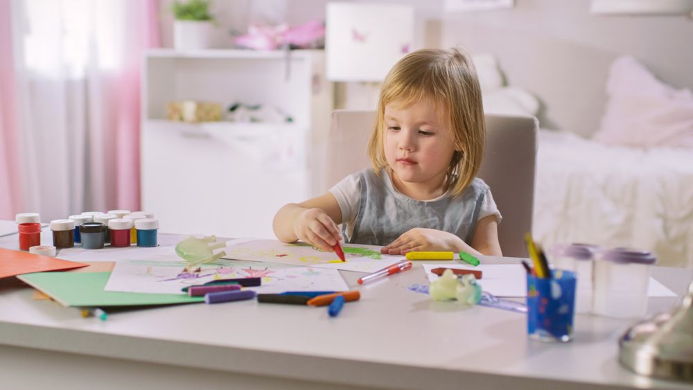 Little Girl Sits at Her Table and Draws with Crayons.