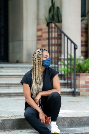 Portrait of nurse on break sitting outside on steps in black scrubs and mask