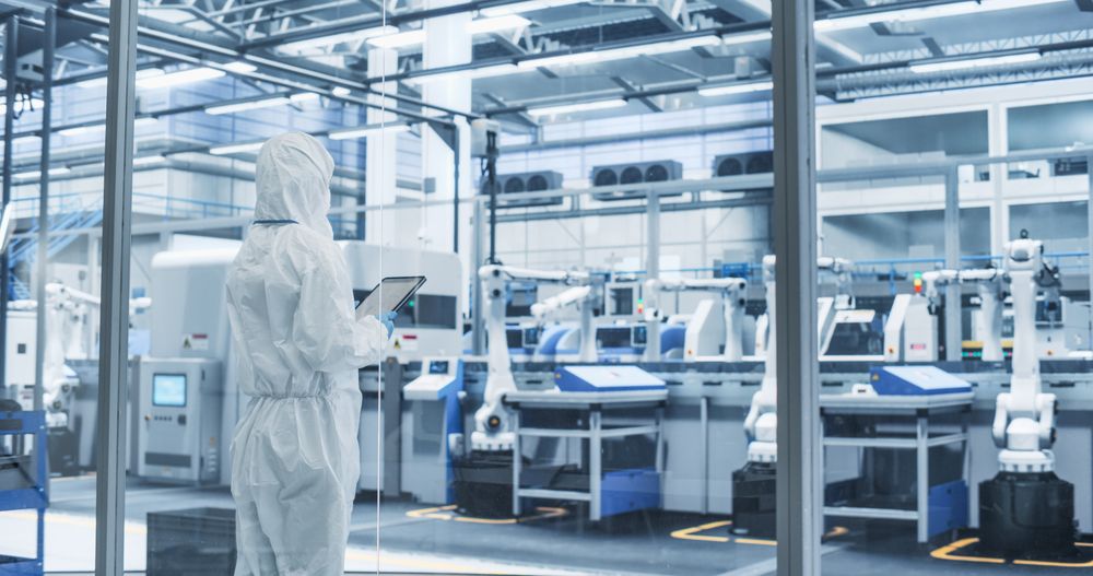 Industrial Scientist Wearing Disposable Protective Suit to Be Protected From Chemical and Biological Dangers. Female Using Tablet Computer, Monitoring Production Process at a Biotechnology Plant