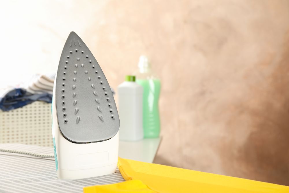 Iron and yellow t-shirt on ironing board, space for text