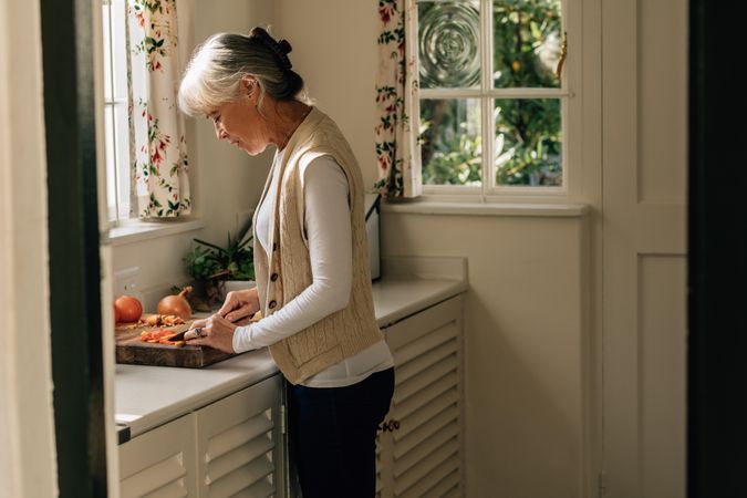 Woman cutting vegetables on a chopping board standing in kitchen