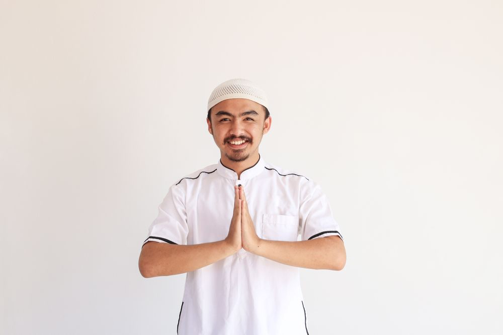 Smiling Young Asian Muslim Man in Baju Koko Standing with Gesturing Eid Mubarak Greeting
