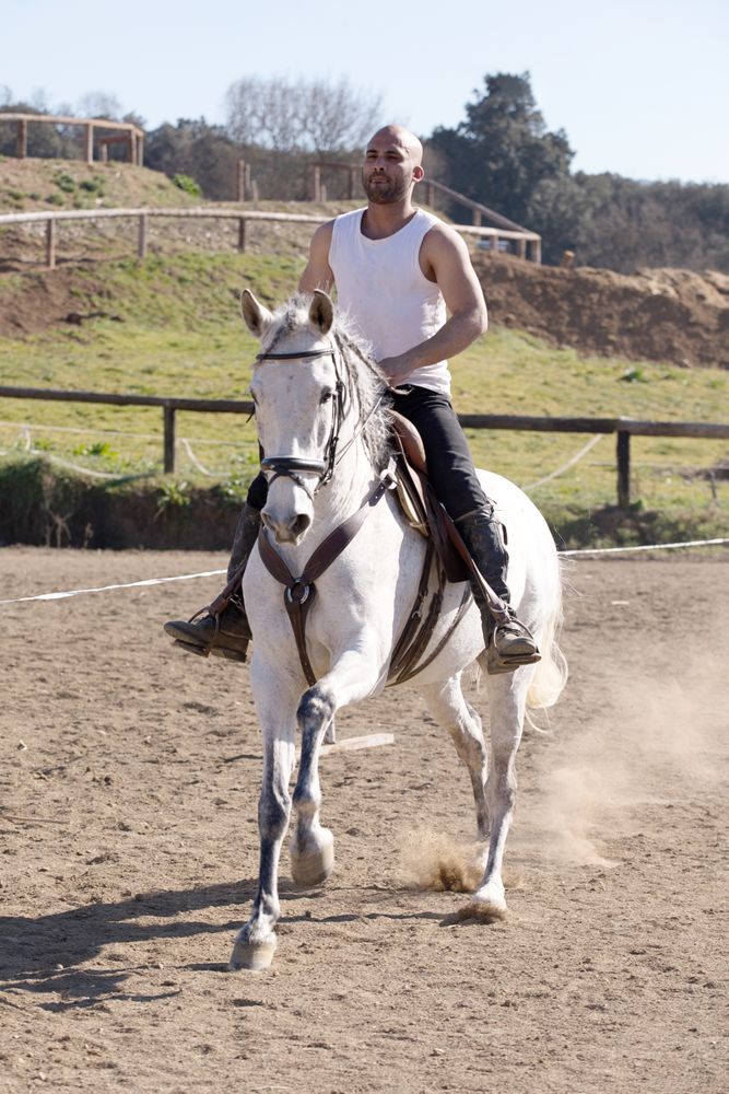 Man in casual riding outfit galloping on horse around paddock