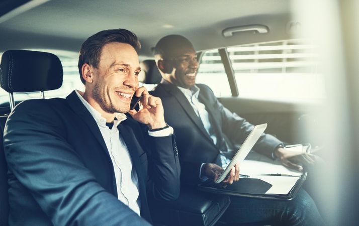 Two businessmen smiling and working while being driven in a luxury vehicle