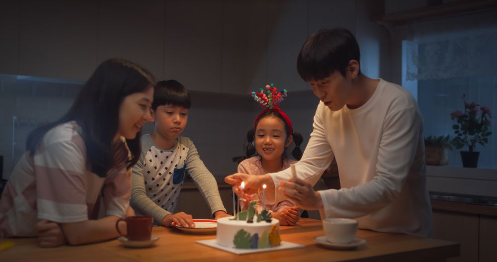 Cute Korean Family Celebrating a Birthday with Cake and Candles at Home During Evening.