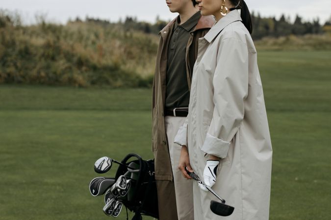 Cropped image of man and woman holding golf club standing on green grass field