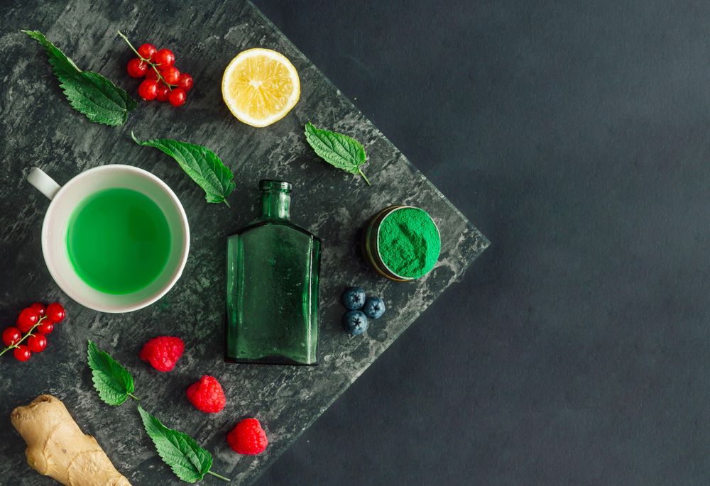 Healthy scene of tea, spirulina powder, nettle leaves, ginger on marble slap on dark background
