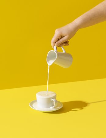 Pouring milk in a cup on yellow background