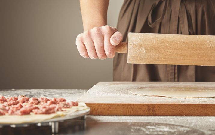 Woman rolling out dough on breadboard for top of ravioli