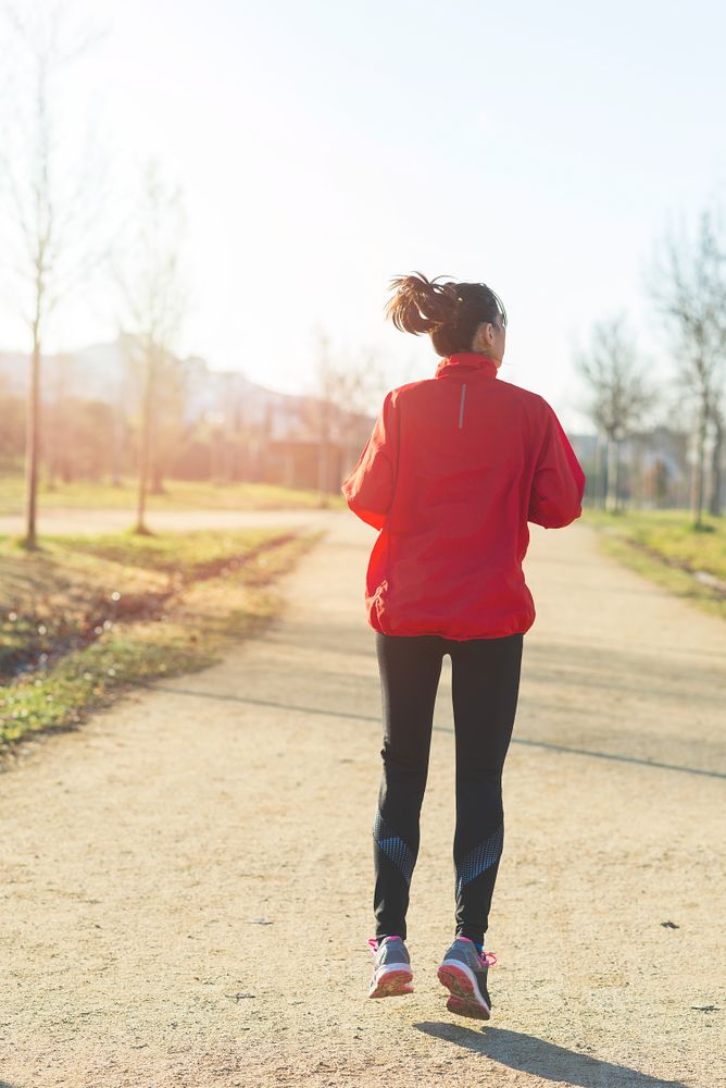 Back of woman running outdoors in a park on sunny day