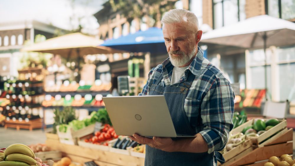 Successful Adult Male Farmer Working on a Laptop Computer, Checking Online Inventory List and Produce Supply