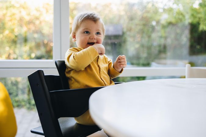 Cute baby boy sitting on high chair at dining table